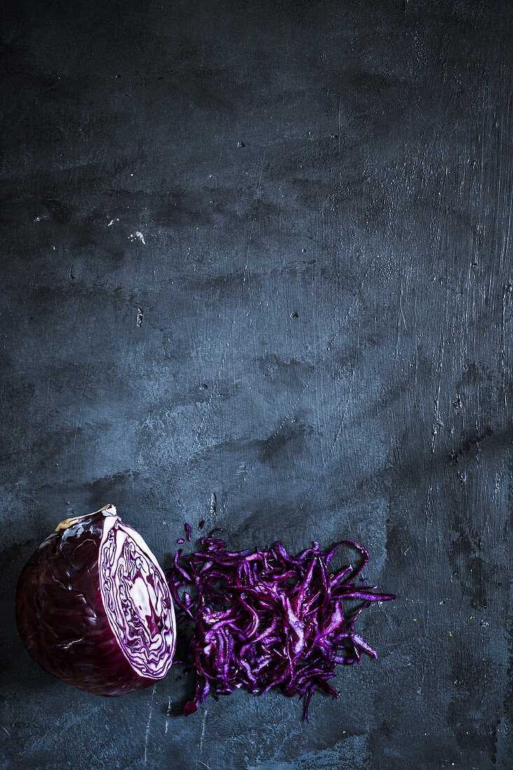 Red cabbage halved and shredded on a dark grey surface