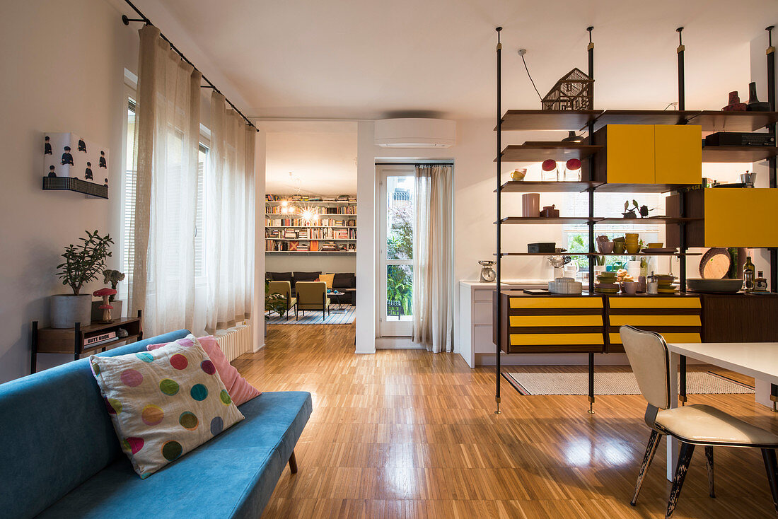 Blue sofa and dining area behind partition shelving with kitchen in background