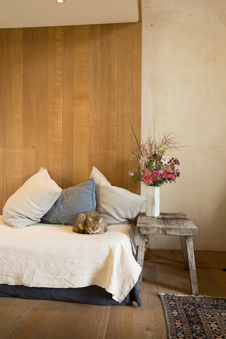 Cat lying on couch, vase of pink flowers and rustic stool