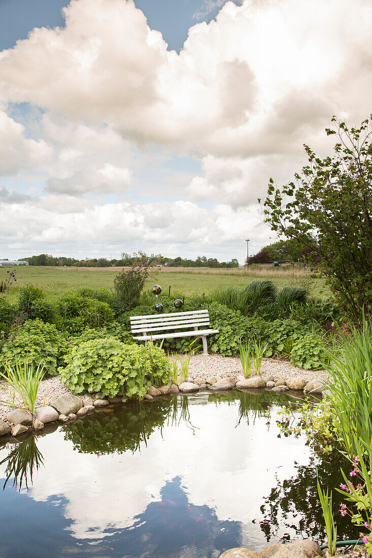 Bench on gravel path next to garden pond (Schleswig-Holstein, northern Germany)