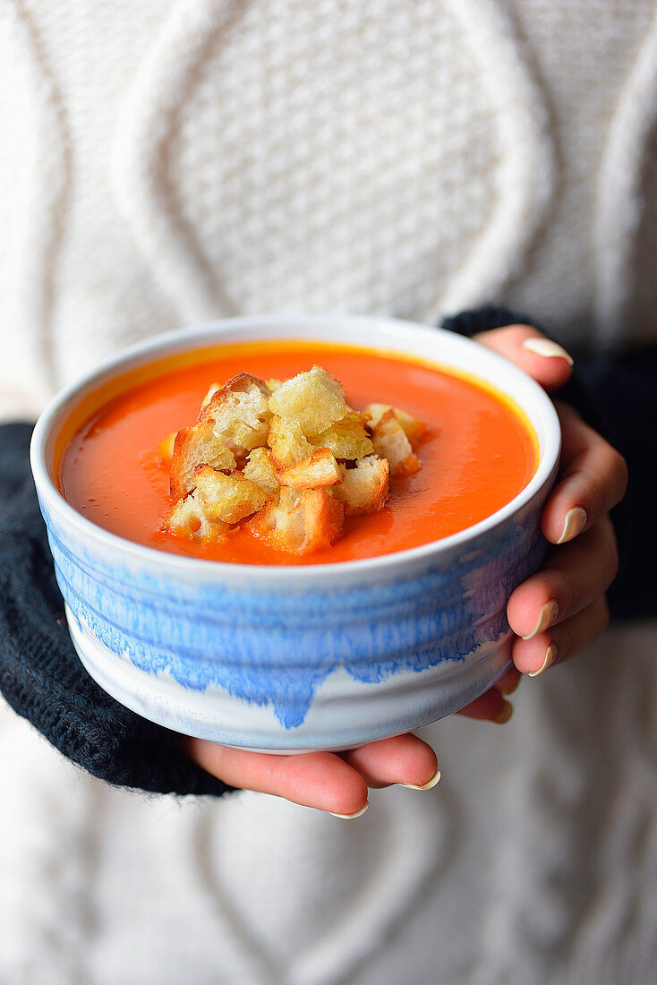 Frau hält einen Teller Kürbissuppe mit Croûtons in der Hand