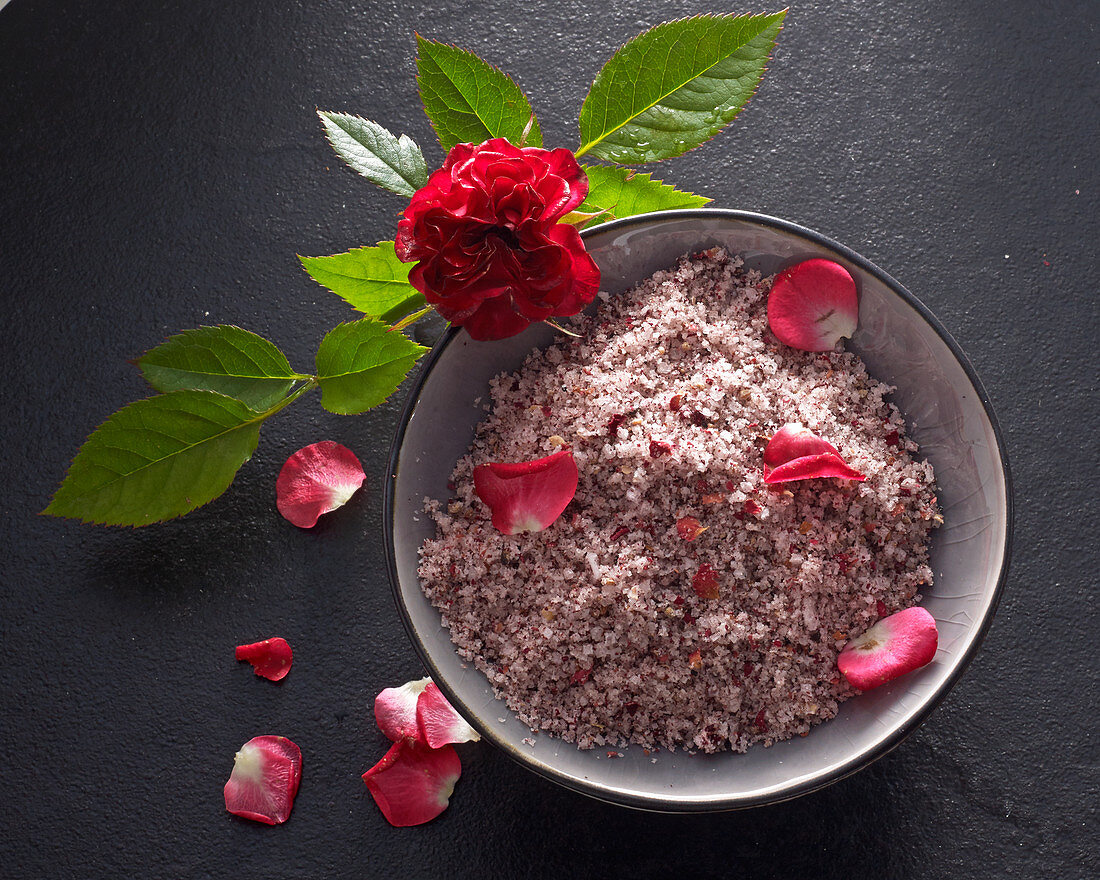 Rosenblättersalz mit Blütenblättern im Keramikschälchen mit einer Rose