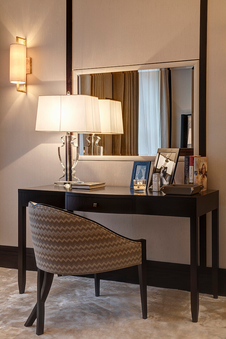 Upholstered chair at dressing table with lamp and photos in bedroom