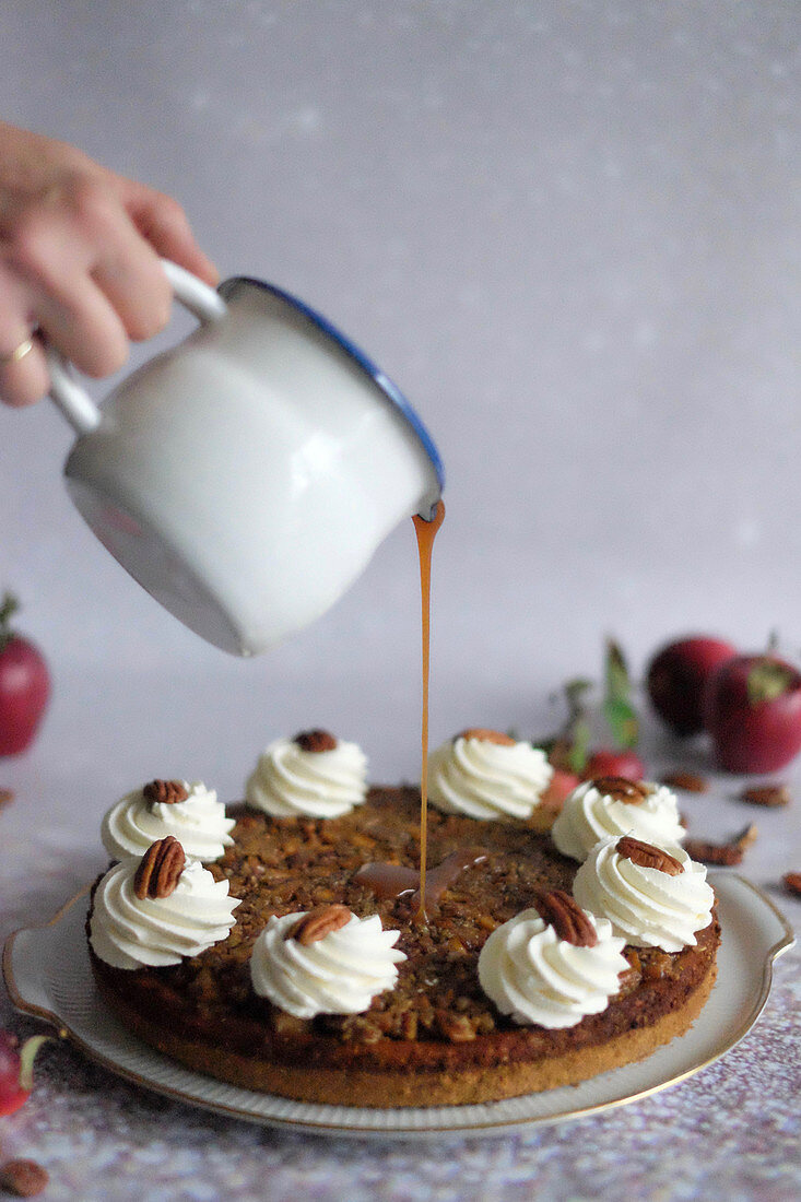 Caramel sauce being poured over an apple and caramel cheesecake