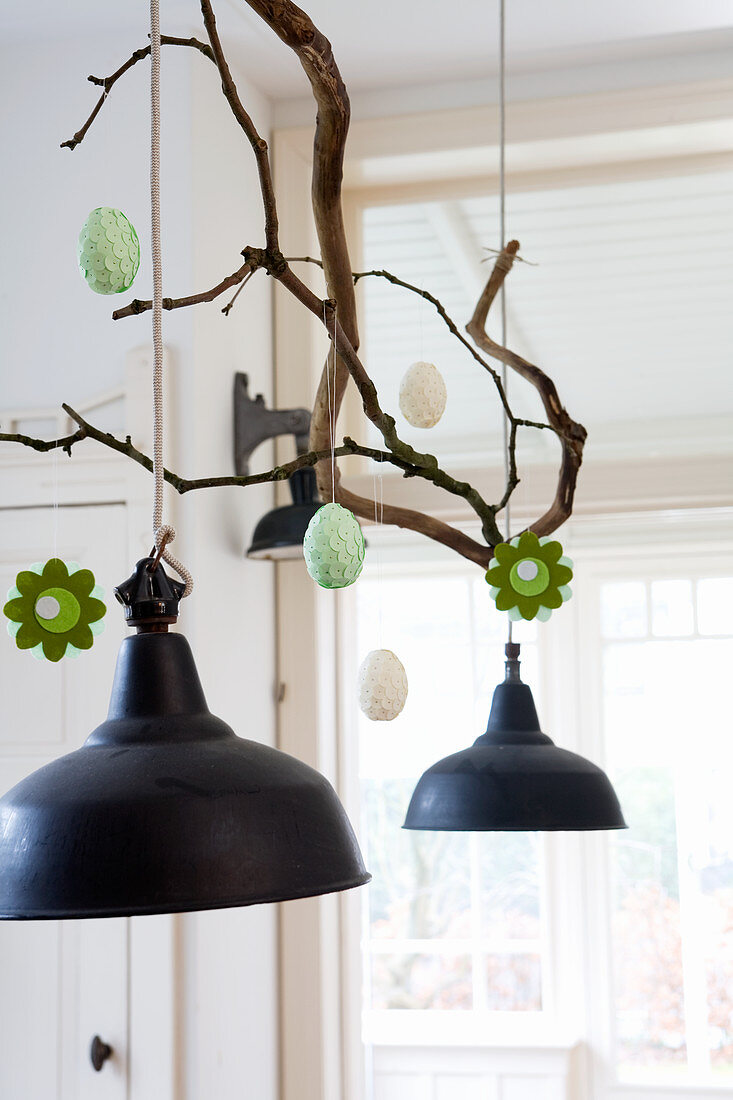 Hand-made felt flowers and Easter eggs hung from branch above pendant lamp