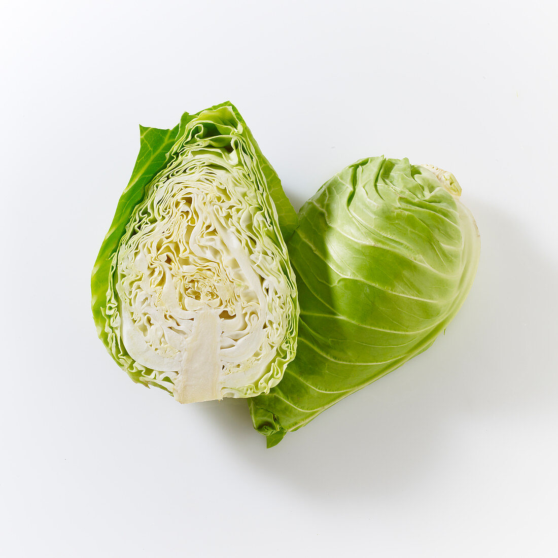 Pointed cabbages, whole and halved, on a white surface