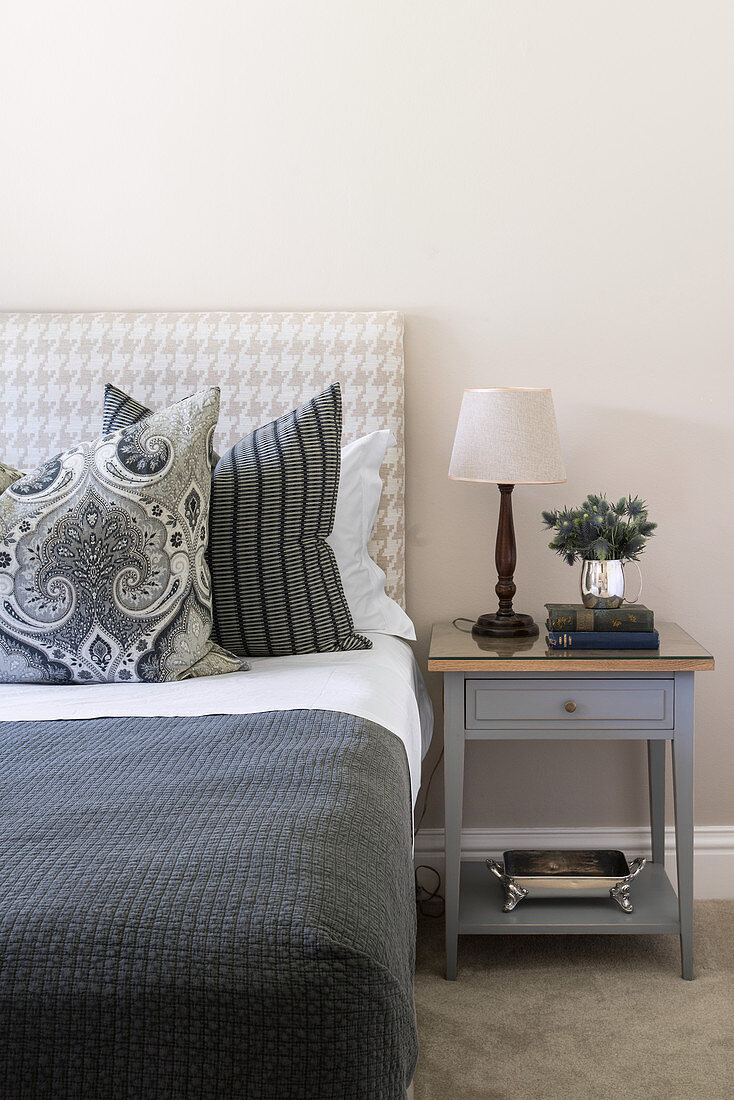 Scatter cushions on double bed with houndstooth headboard and bedside table in simple guest room