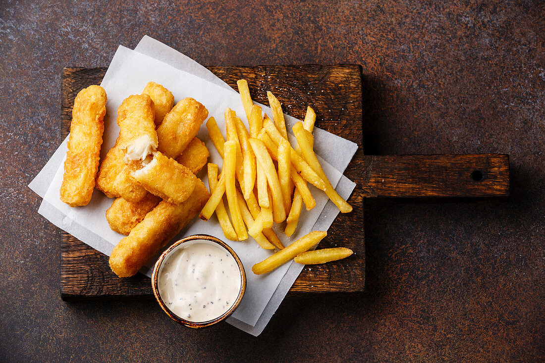Fish fingers and Chips, british fast food with tartar sauce on dark background