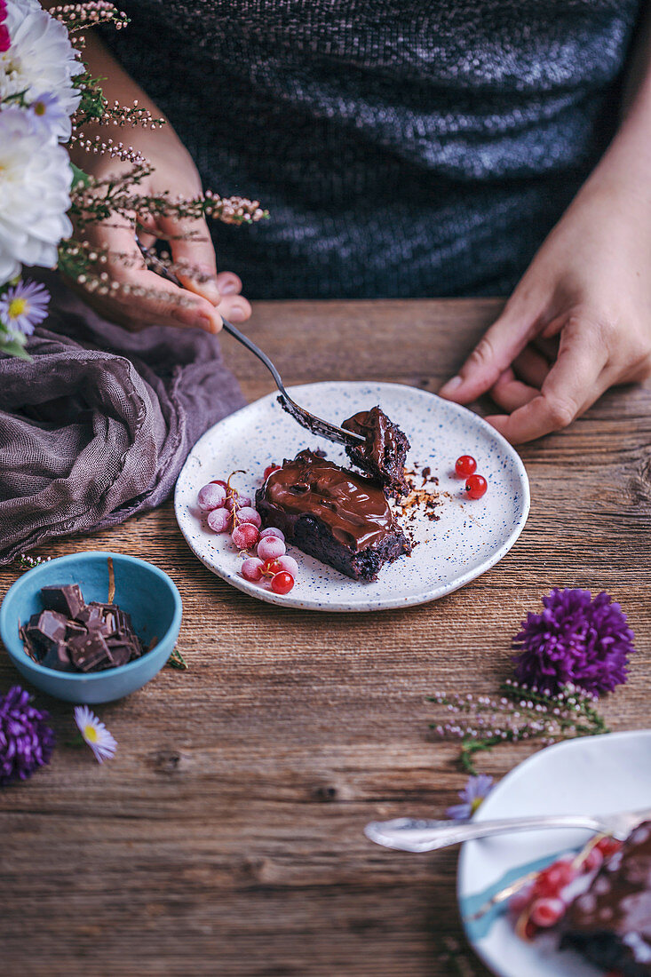 Woman eating chocolate sweet potato brownies served on dessert plates on rustic wooden table