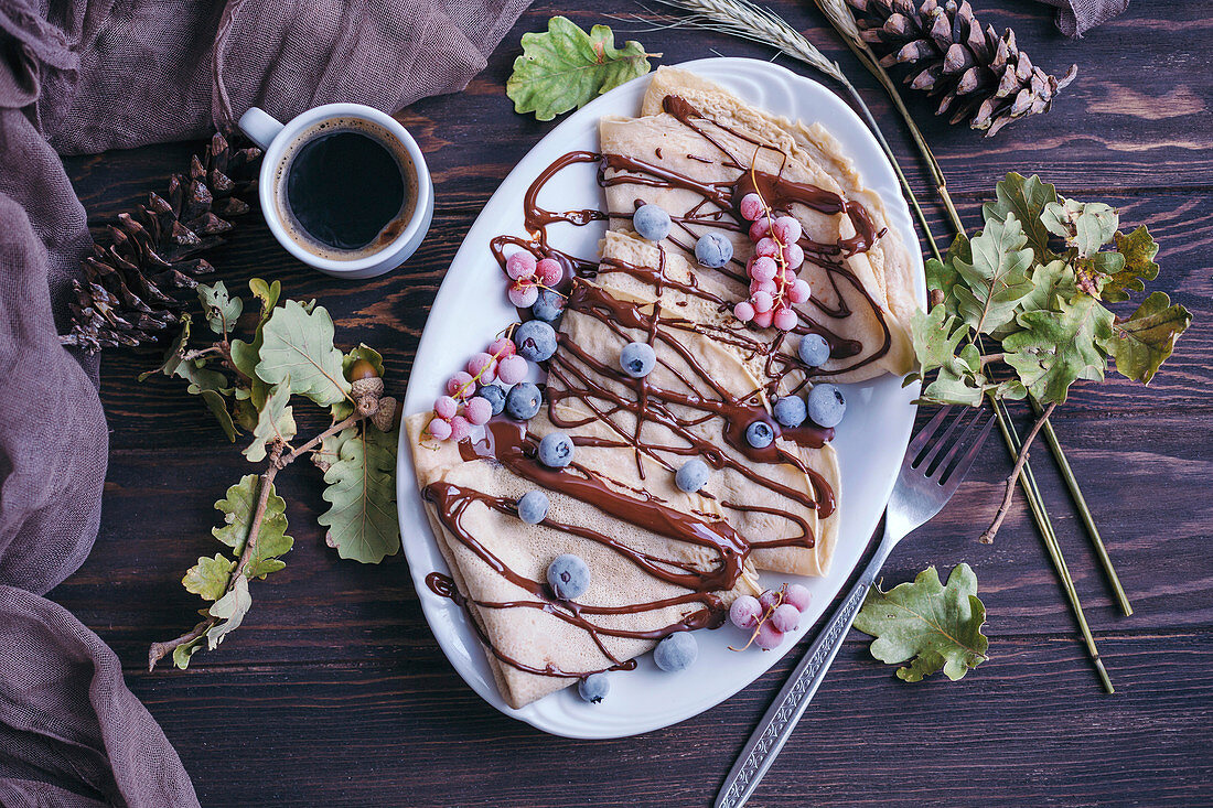 Crepes with chocolate drizzle and frozen berries and cup of black coffee