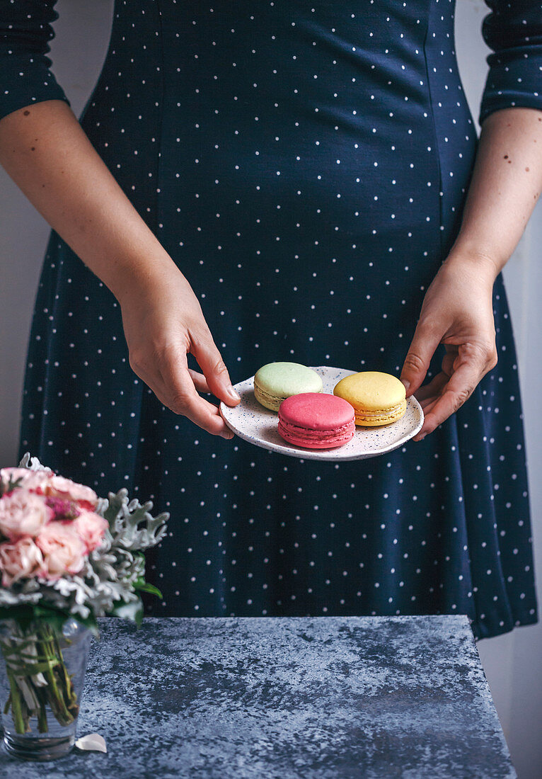 Frau hält einen Dessertteller mit drei verschiedenen Macarons