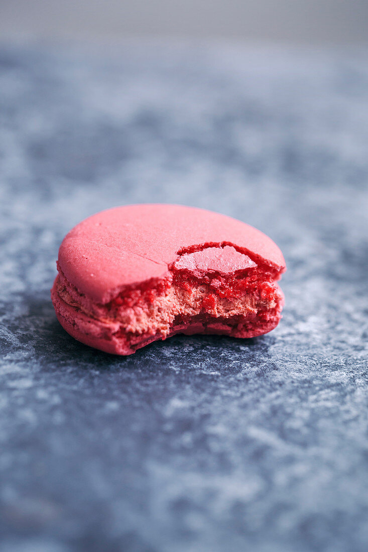 Half eaten pink macaron on grey background