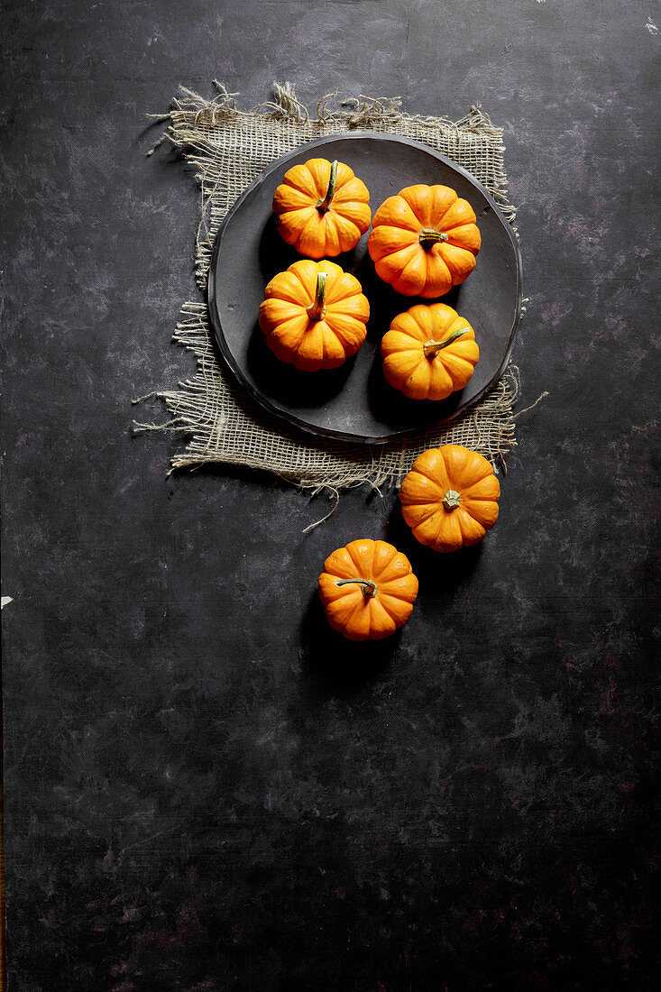 Small orange pumpkins on a black plate with a black background (top view)