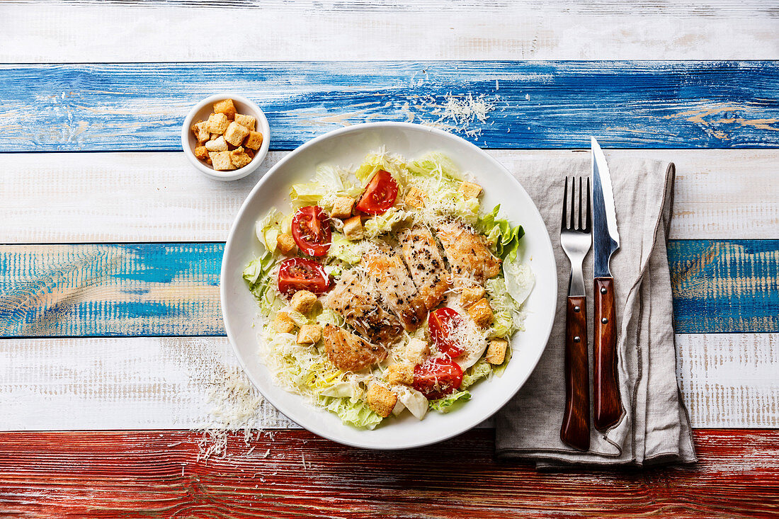 Caesar salad with chicken breast and croutons on wooden background