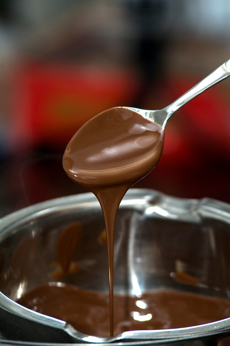 Geschmolzene Schokolade fliesst von Löffel in Schüssel