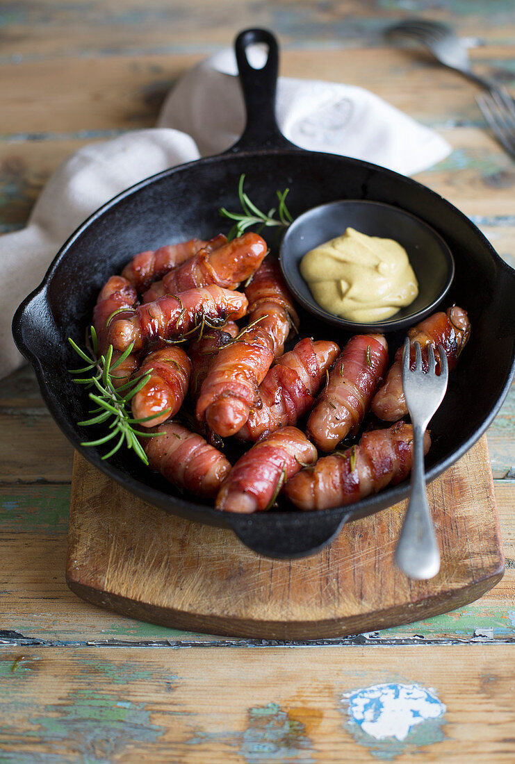 Bacon-wrapped chipolata sausages with mustard in a pan