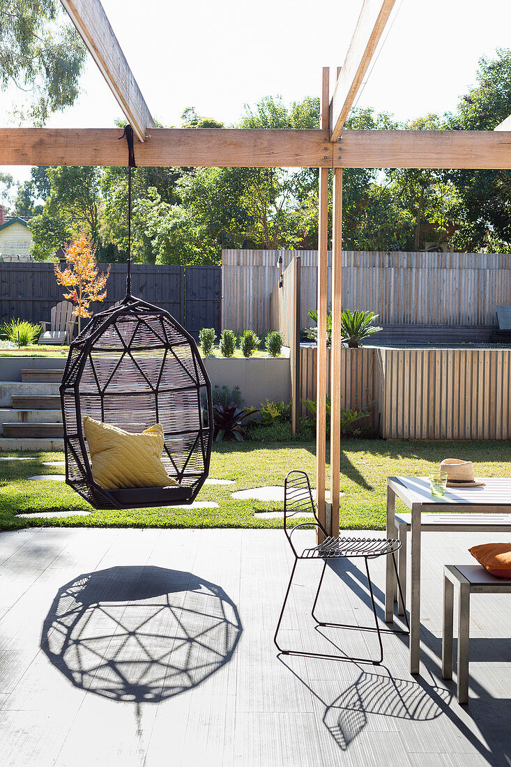 Hammock chair on sunny terrace with pergola in modern garden