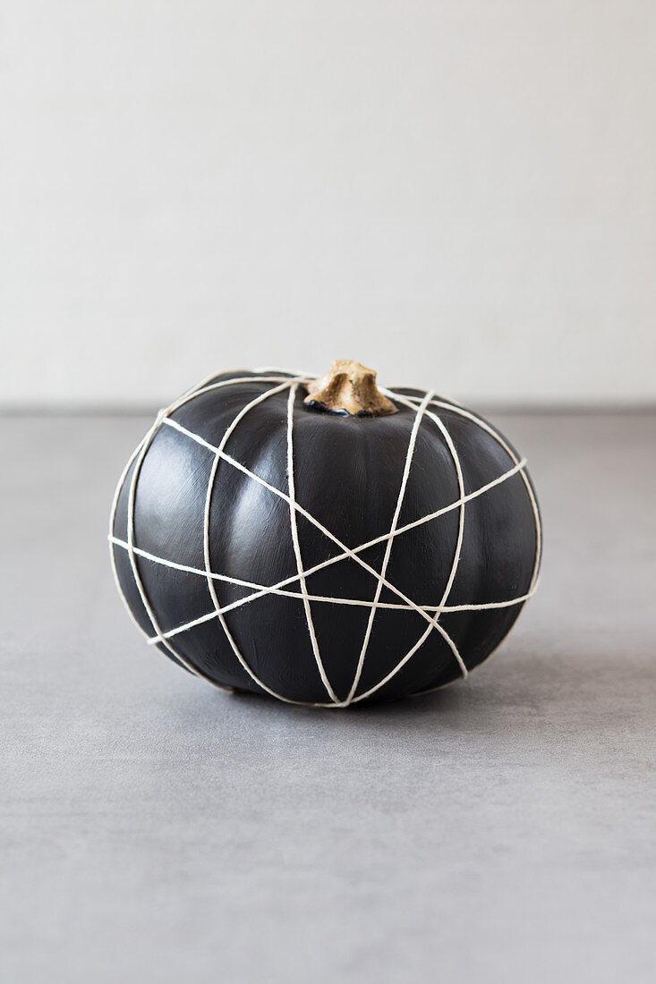 Black-painted pumpkin wrapped in criss-crossing string