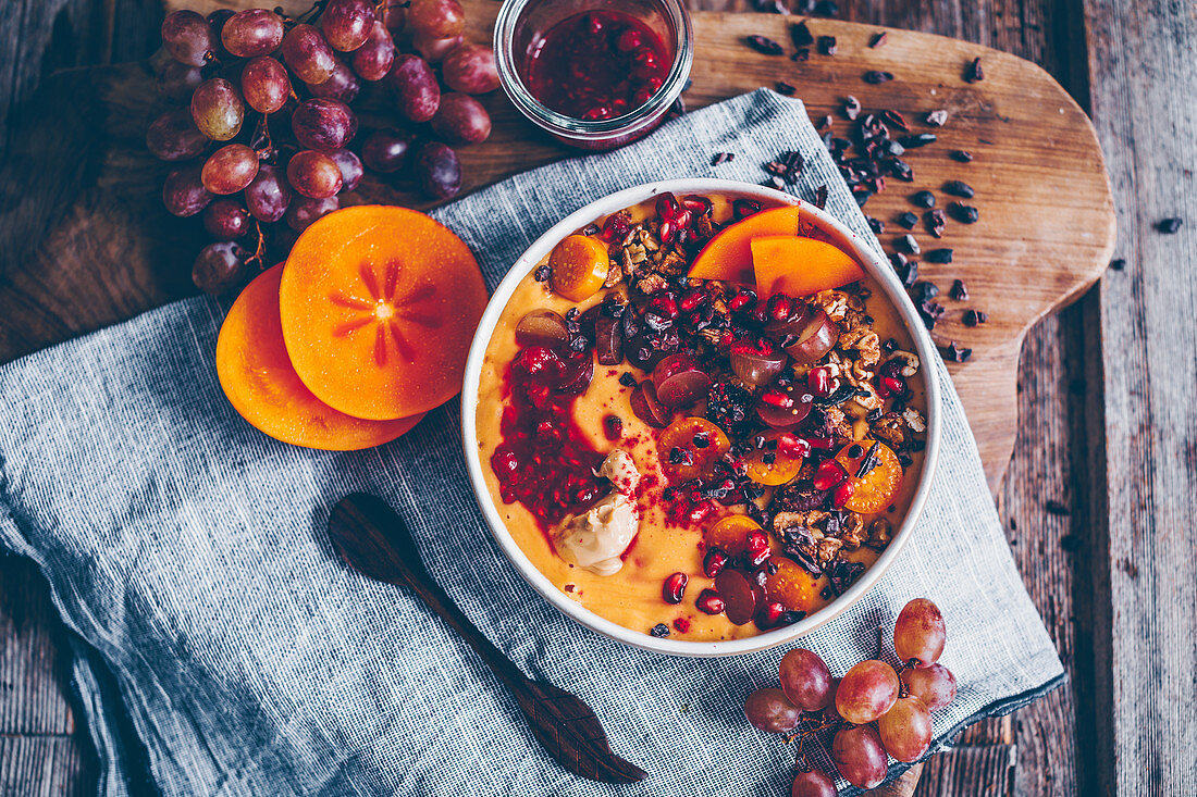 Smoothie bowl with kaki, papaya, pomegranate seeds, grapes, cacao nibs, raspberry compote, granola and physalis