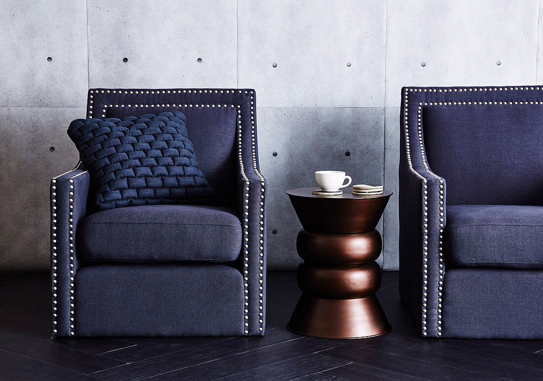 Copper-colored side table between blue armchairs with upholstery nails