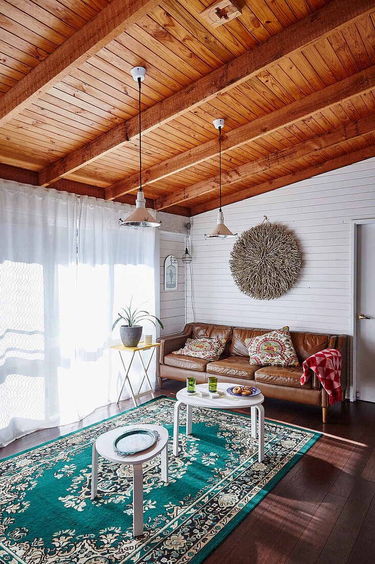 Braune Ledercouch und weiße Tische im Wohnzimmer mit Holzbalkendecke