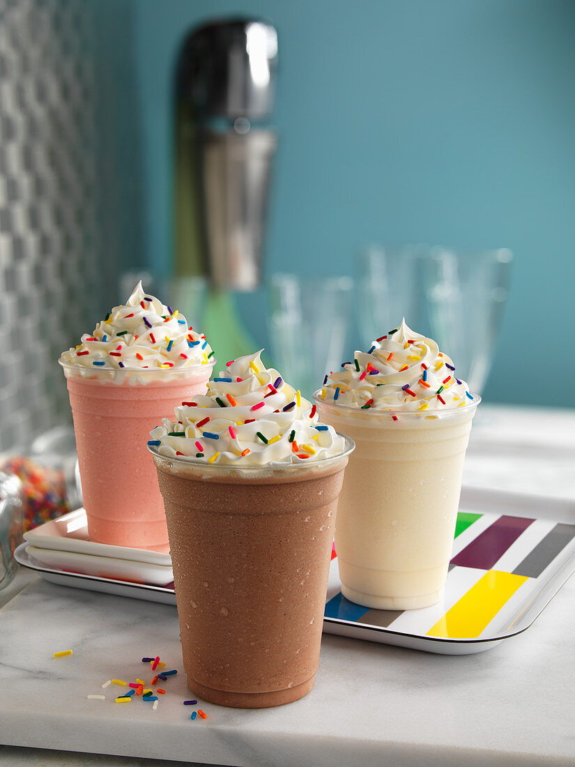 Three different milk shakes with cream and colourful sugar sprinkles