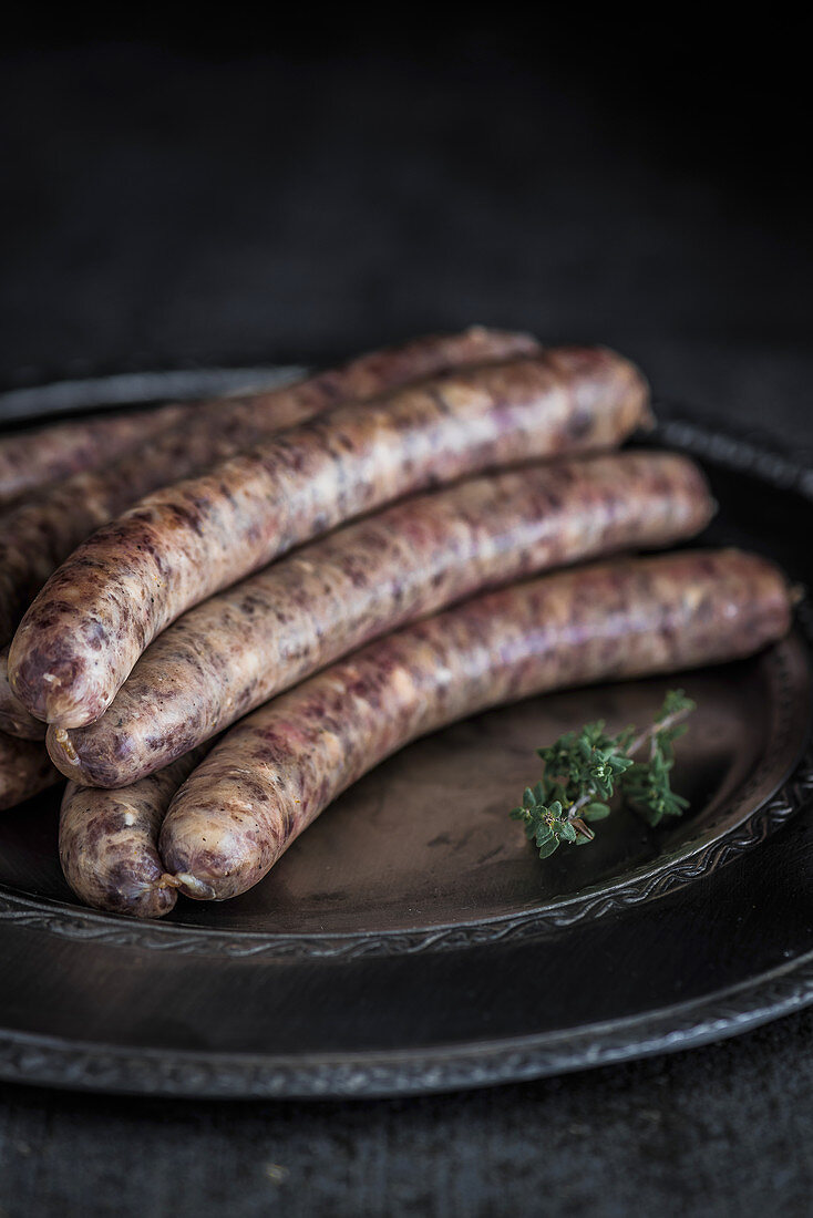Wagyu bratwurst on a serving dish with a thyme sprig