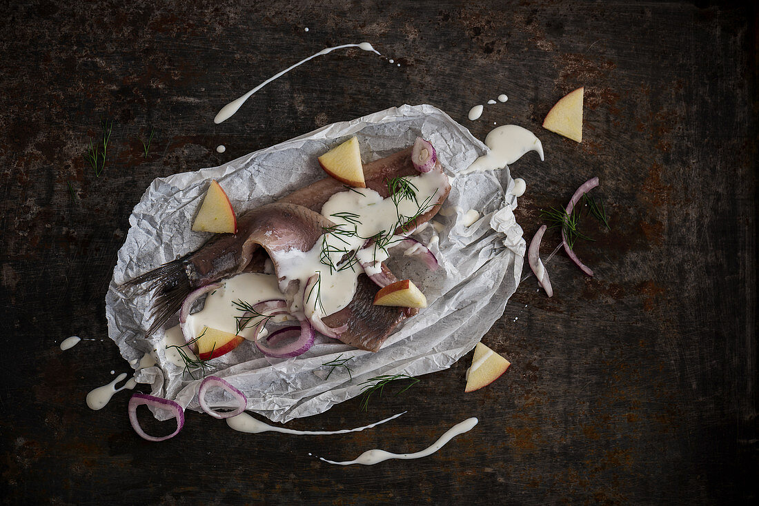 Herring fillets with yoghurt sauce, pieces of apple, shallots, and dill on parchment paper
