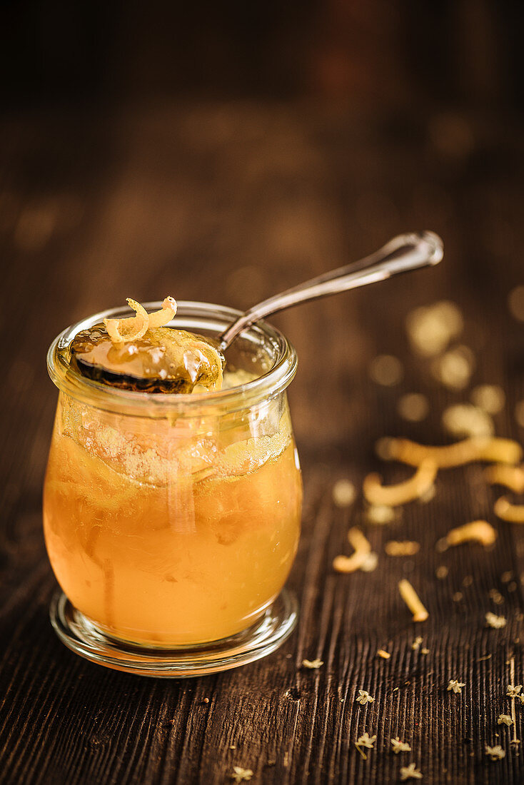 Orange marmalade with orange zest in a glass jar on a wooden background