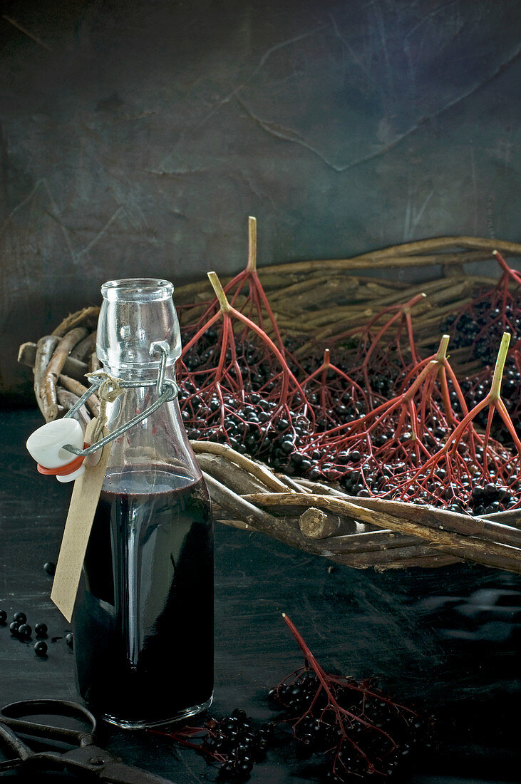 A bottle of elderberry juice, fresh elderberries in a wicker basket