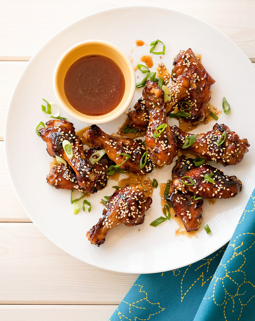 Grilled honey and sesame seed chicken wings on a white wooden table