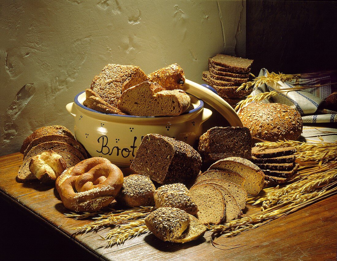 Stillleben mit dunklen Brotsorten, Brezen, Brötchen, Getreide