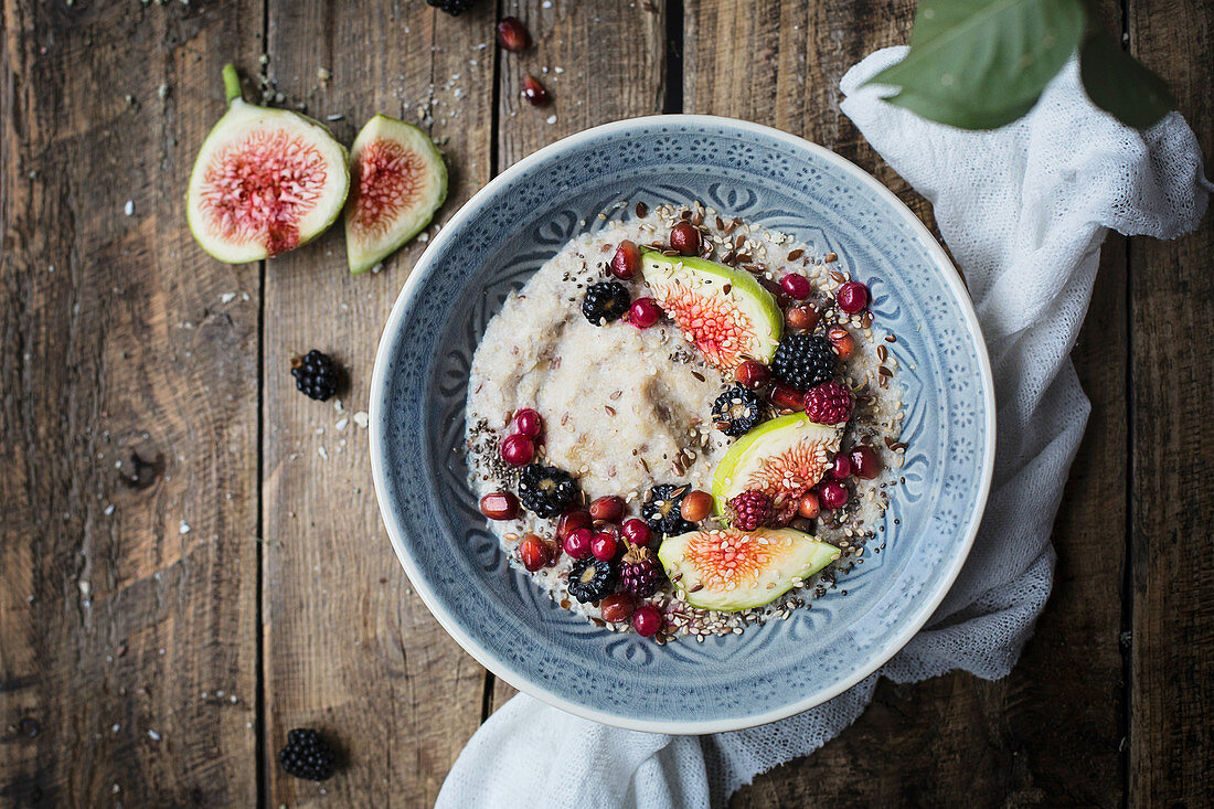 Breakfast porridge with figs and blackberries in a bowl on a rustic wooden table
