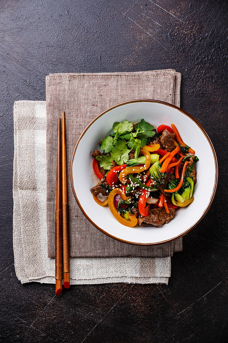 Szechuan beef stir fry with vegetables in bowl on dark background