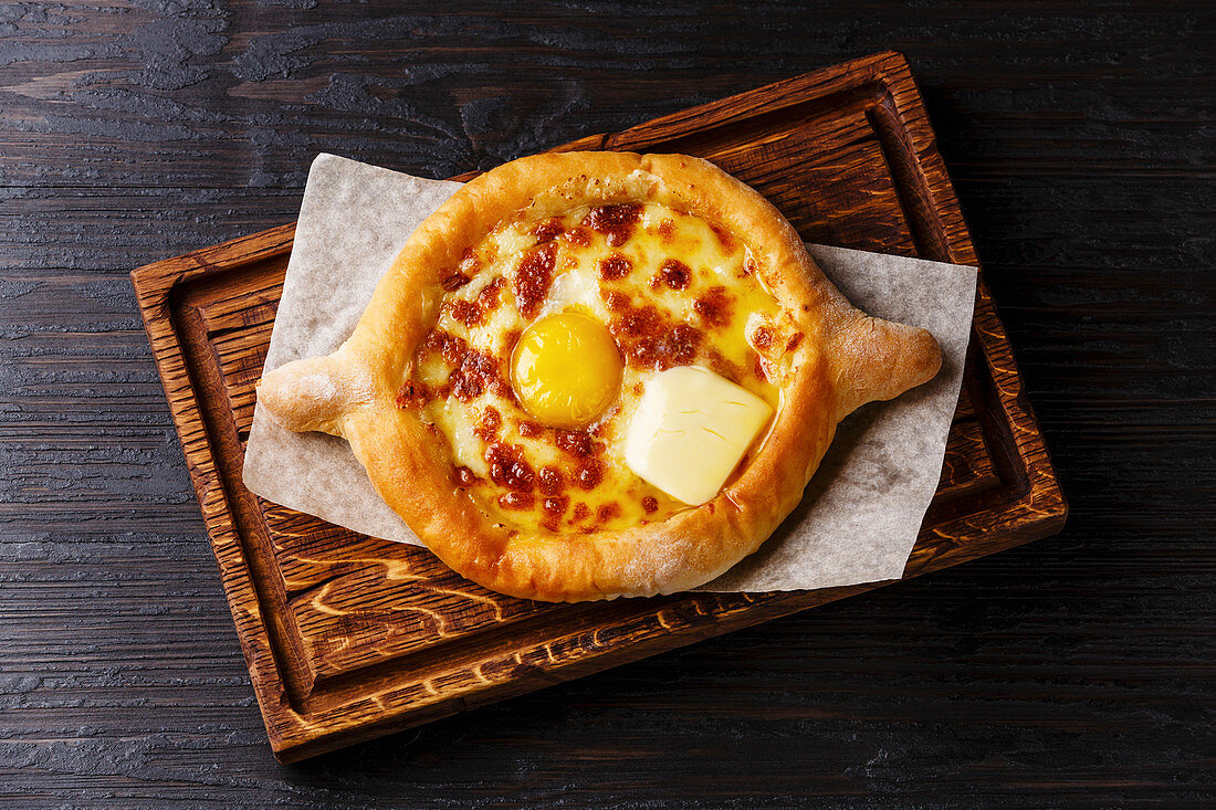 Georgian cheese pastry Ajarian Khachapuri serving size on burned black wooden background
