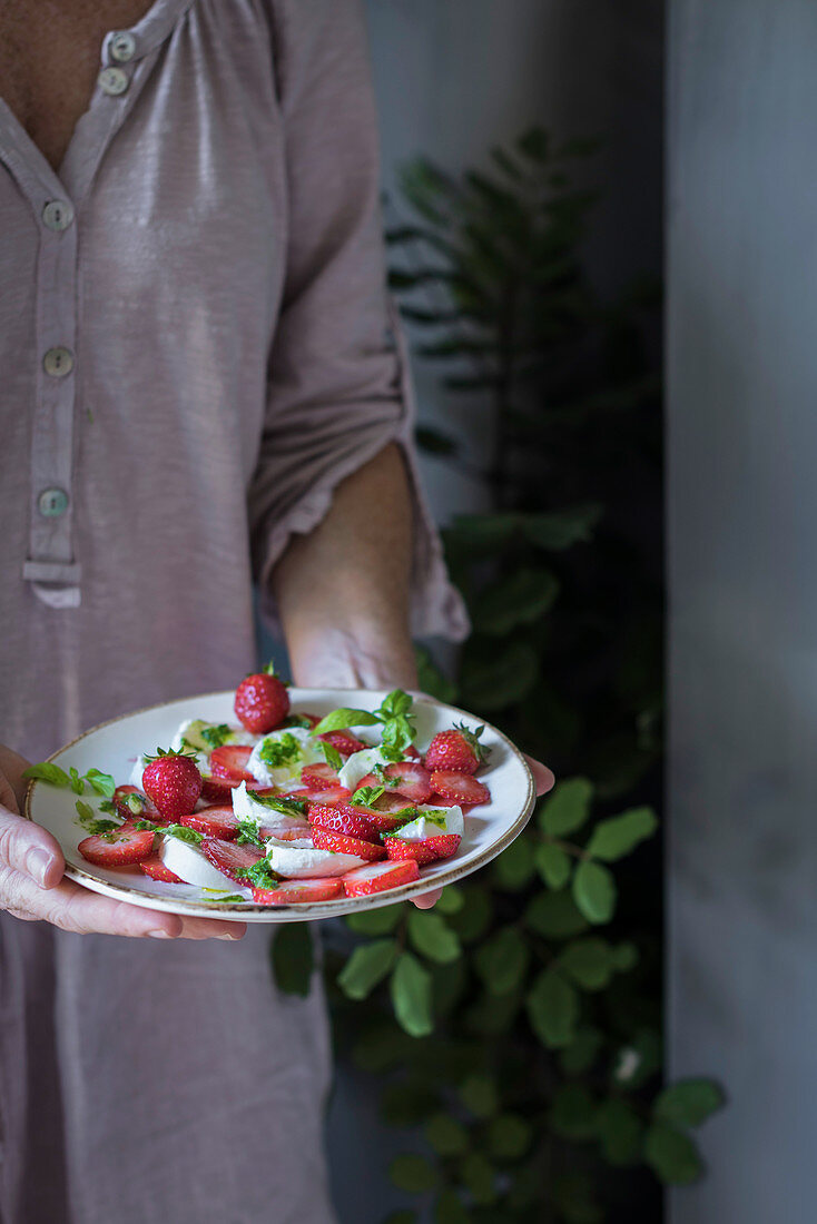 Frau hält Teller mit Erdbeer-Mozzarella-Salat in den Händen