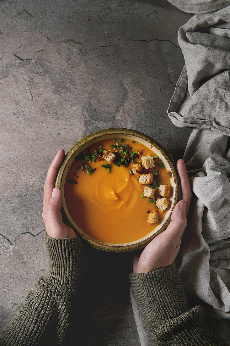 Bowl of vegetarian pumpkin carrot soup served with saffron salt, croutons and onion