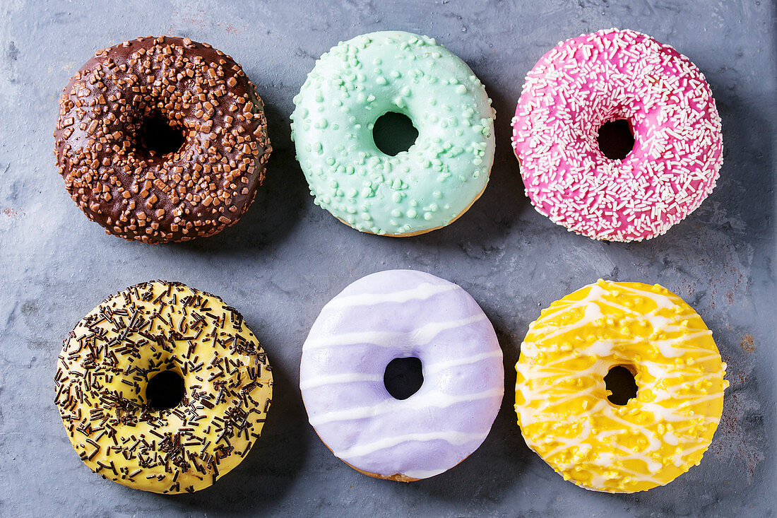 Variety of colorful glazed donuts over gray metal texture background