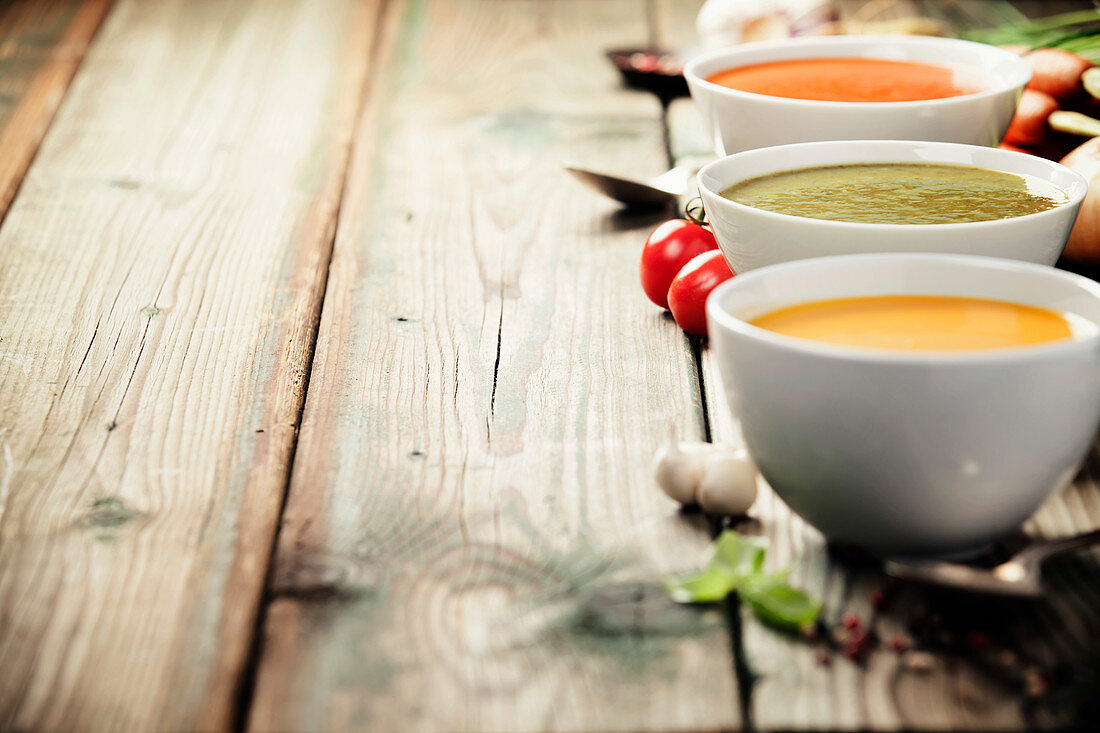 Variety of cream soups - tomato, broccoli and pumpkin soups over wood background