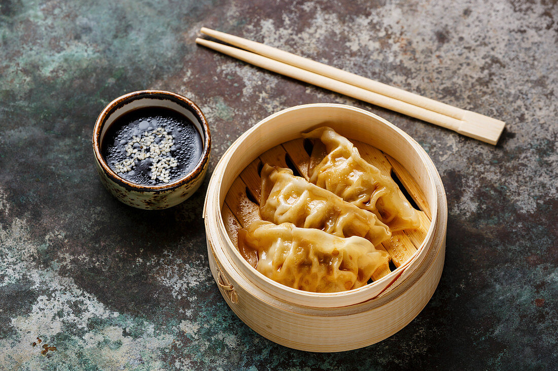 Steamed dumplings Gyoza in bamboo steamer with chopsticks and sauce on metal background