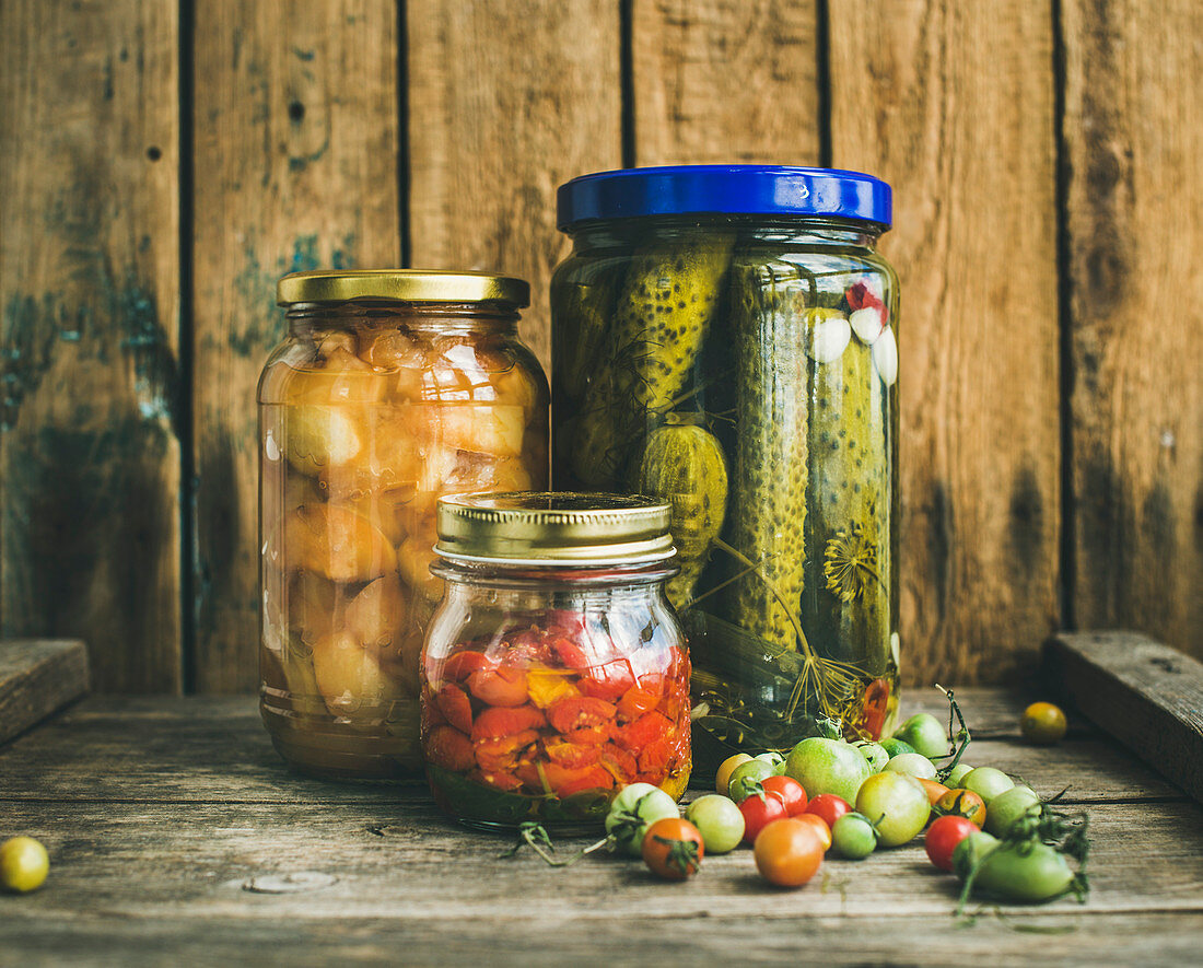 Eingelegtes Gemüse und Herbstfrüchte in Gläsern vor Holzhintergrund