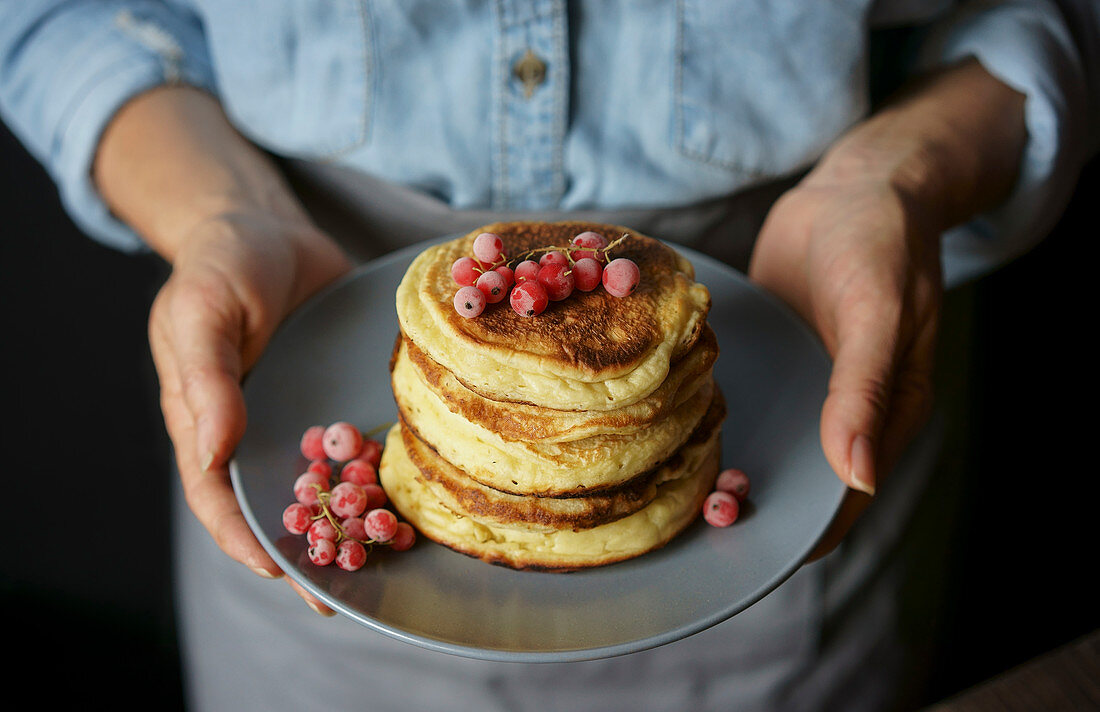 A woman holding a plate of stacked pancakes
