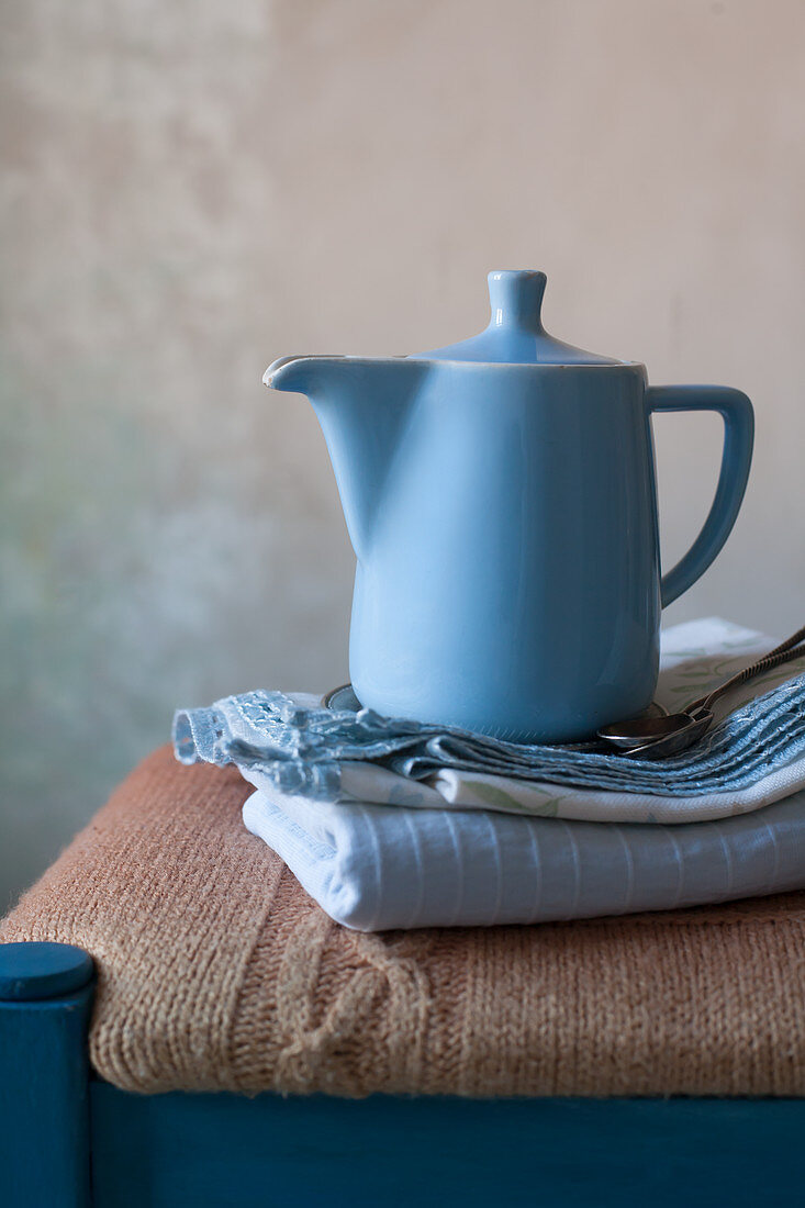 Blaue Kaffeekanne und ein Stapel Tücher auf einem Hocker