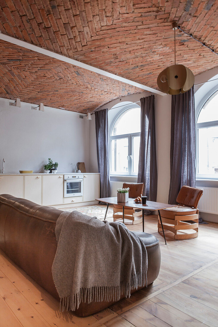 Leather sofa, coffee table and designer leather chair in open-plan living room with brick ceiling and kitchen counter in background