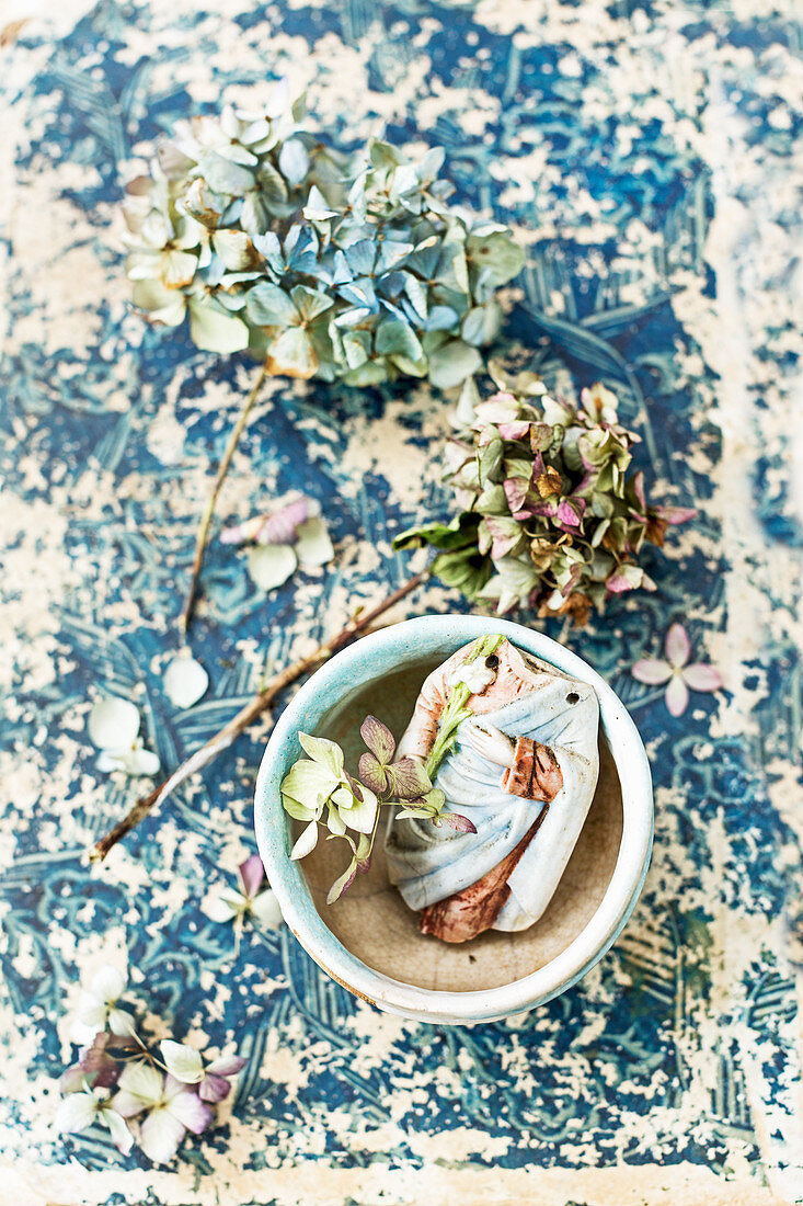 Dried hydrangea flowers and ceramic shards in bowl on old book cover