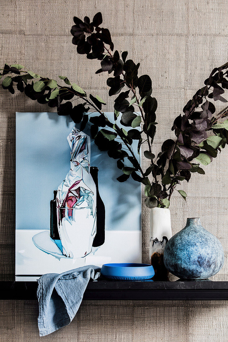 Picture and vase with branches of leaves against wall with designer wallpaper