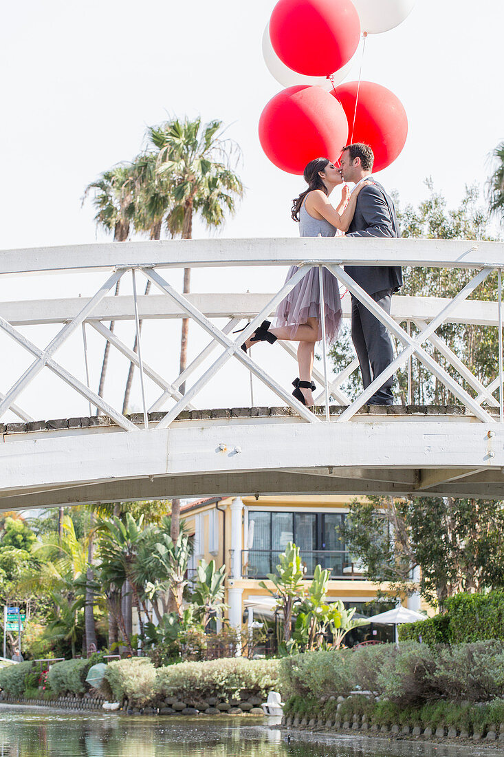 A couple with balloons kissing on a bridge