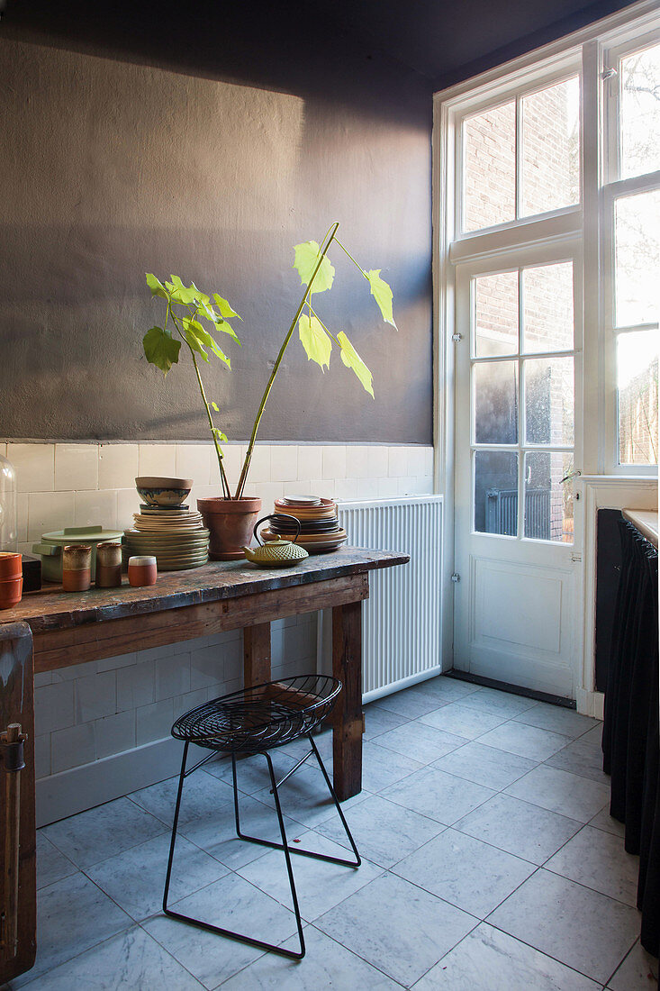 Alter Holztisch mit Geschirr und Zimmerpflanze in Küche mit dunkler Wand