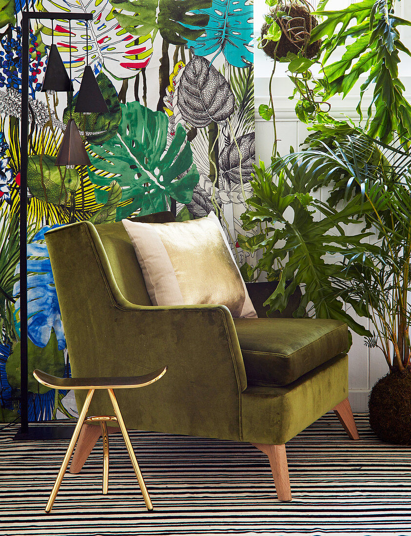 Gilt stool and green velvet armchair in front of leaf-patterned wallpaper