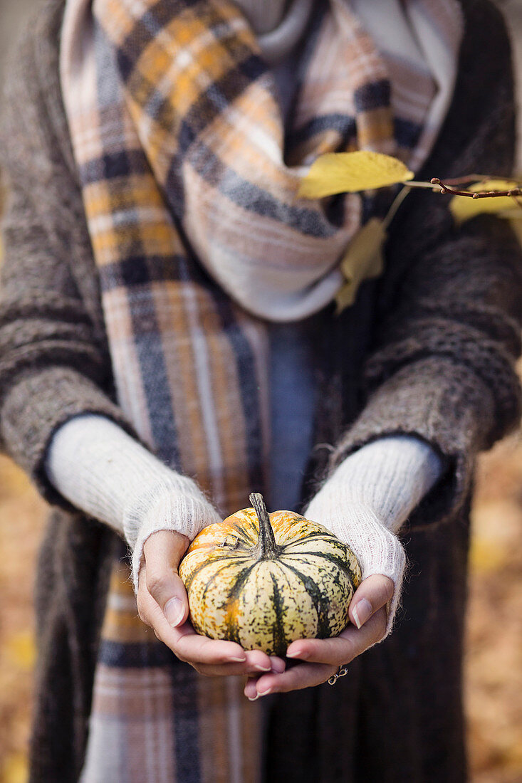 Herbstlich gekleidete Frau hält kleinen Kürbis in den Händen